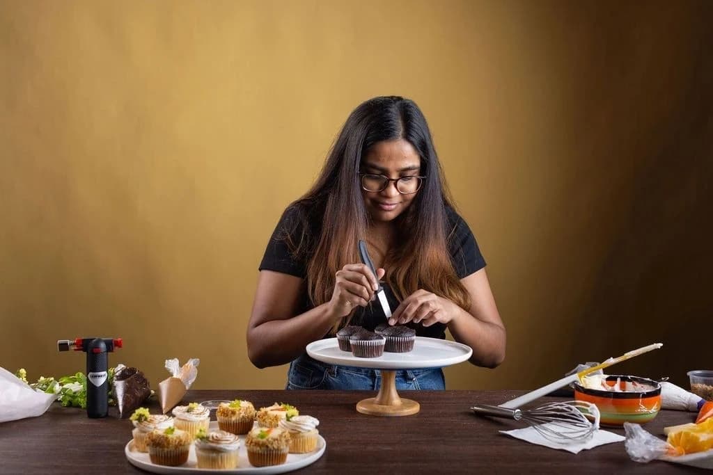 A baker decorating cupcakes against a coloured Studio7 backdrop.