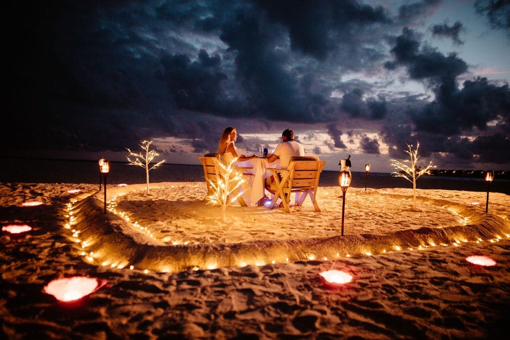 Couple at heart-shaped candlelit beach setup under stormy sky