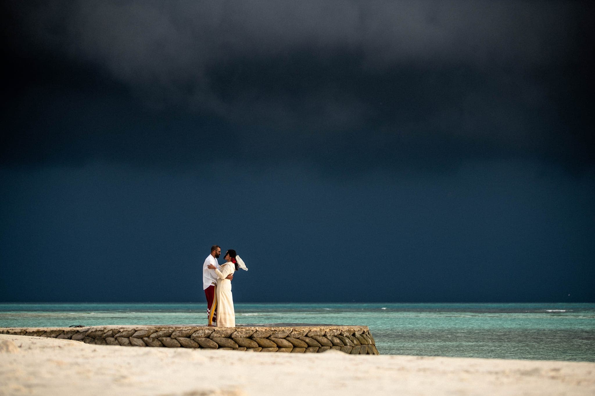 Couple embracing on beach jetty under dramatic storm sky